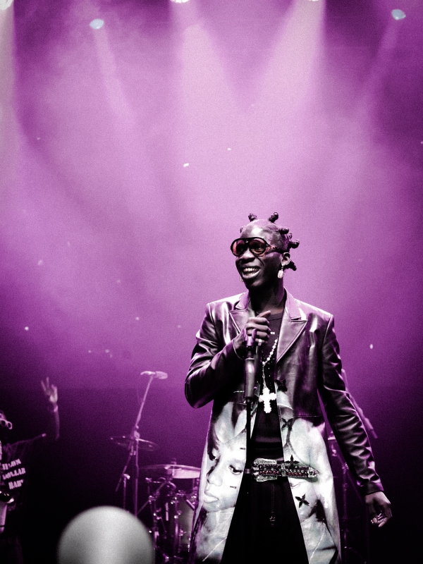 Close-up of Seyi Vibez smiling in a patterned blazer performing under bright purple stage illumination. — concert photography London by Lamss Media